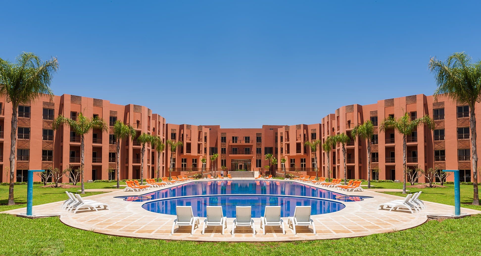 The pool with sun loungers, lawns and palm trees