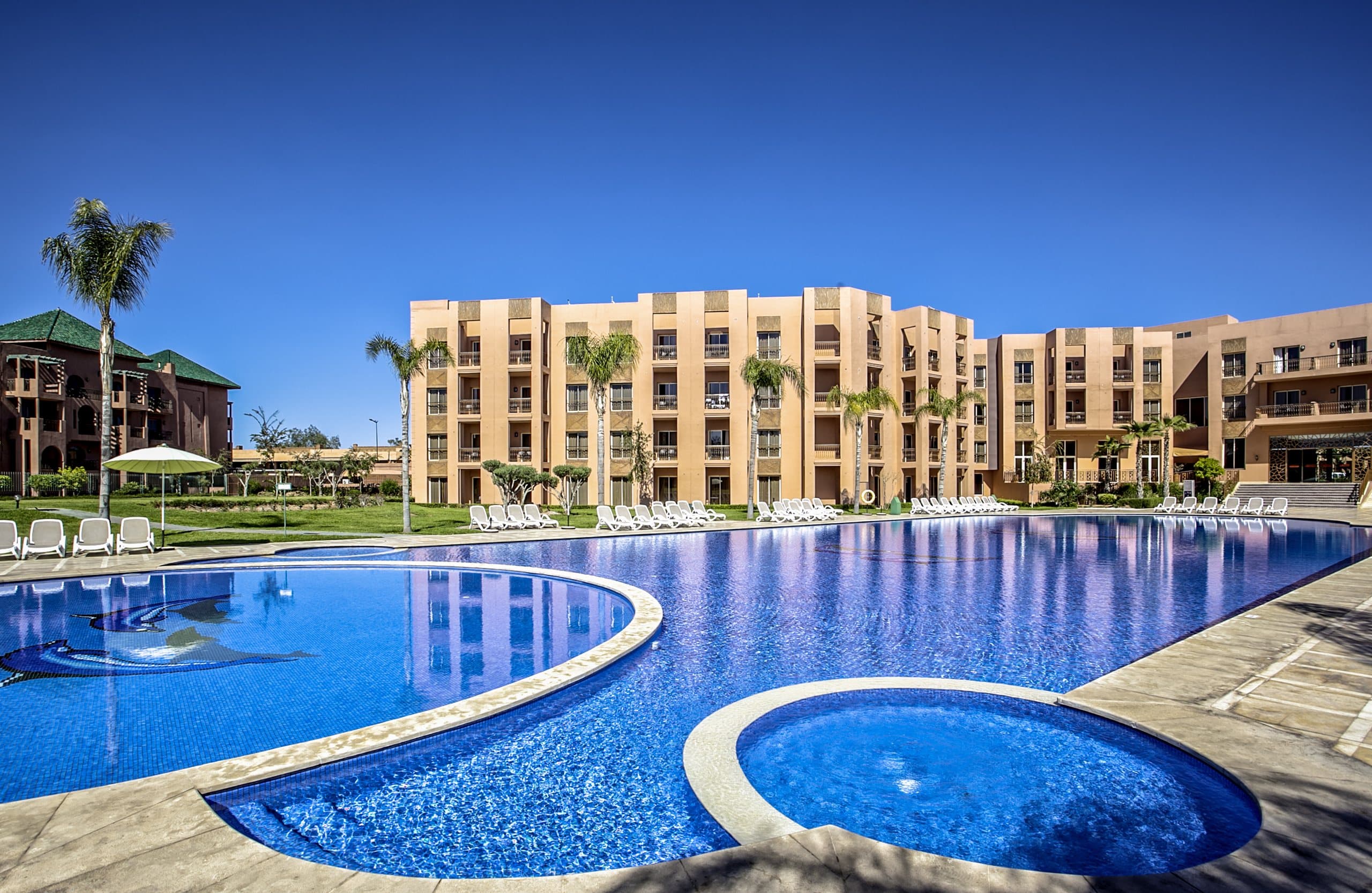 The main pool, palm trees and the hotel's terracotta buildings under a deep blue Marrakesh sky